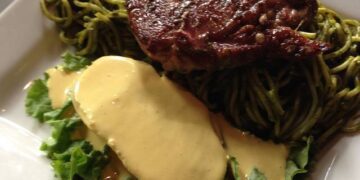 Tallarines verdes acompañados de una sábana de bistec apanado y papa amarilla con crema a la huancaína